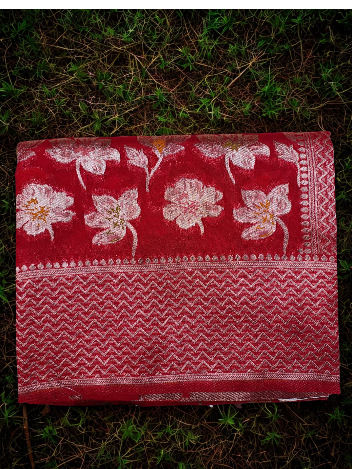 Red fabric with golden floral patterns on a grassy background